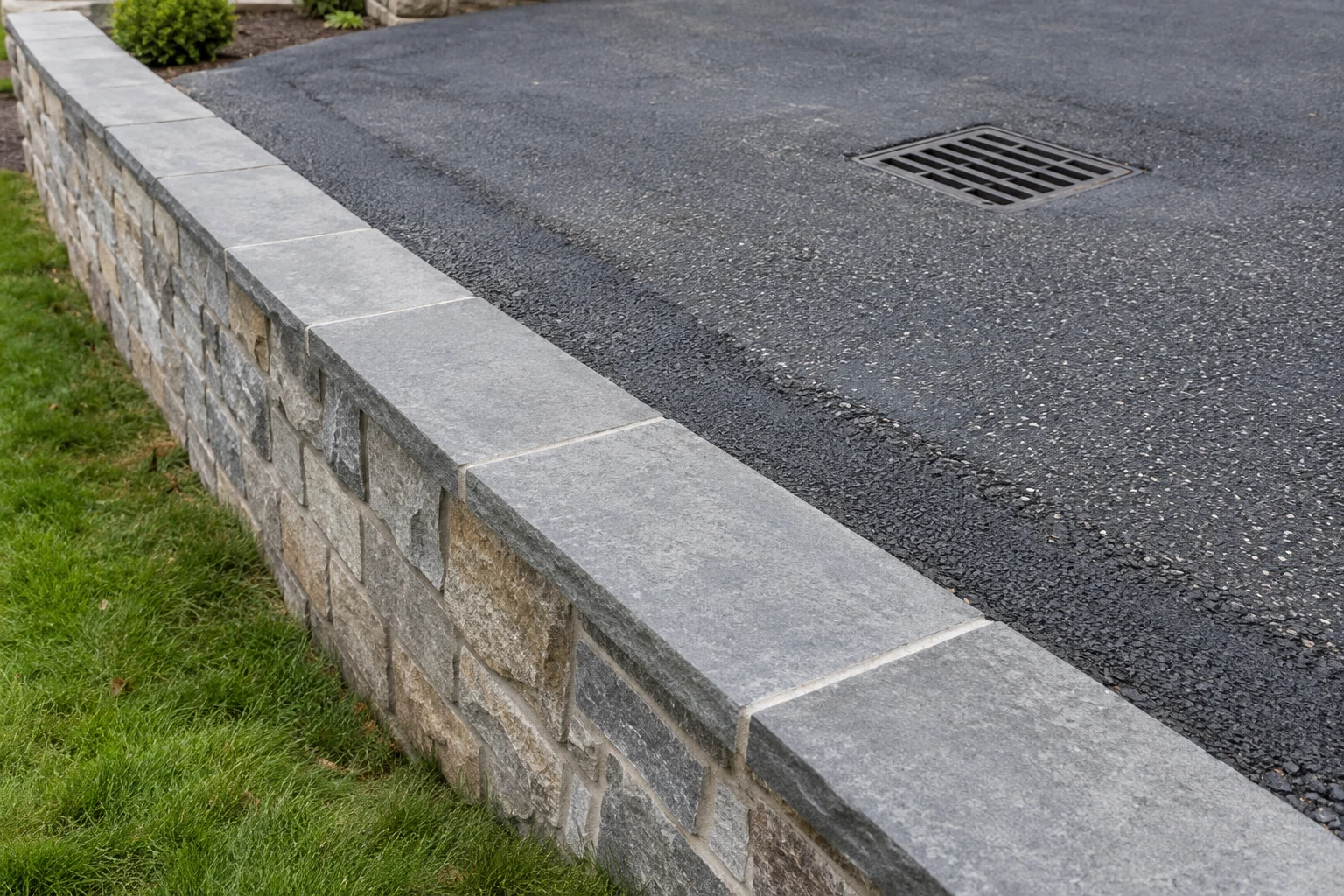 Retaining wall cap beside a driveway restoration seam and grated drainage inlet
