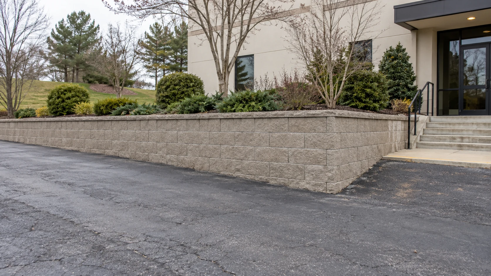 Low block retaining wall supporting a planted commercial property edge beside asphalt access
